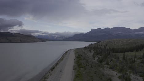 Mountains-lake-roadside-highway-light-traffic-with-partly-cloudy-day-and-sunlight-behind-clouds