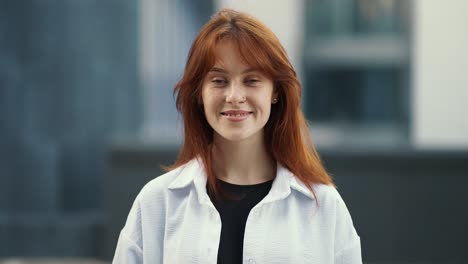 a young girl with a red hair in a white t-shirt smiling and looking straight ahead