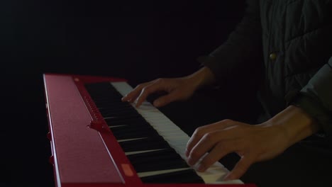 primer plano estático de una persona tocando un teclado de piano con ambas manos en una habitación con poca luz