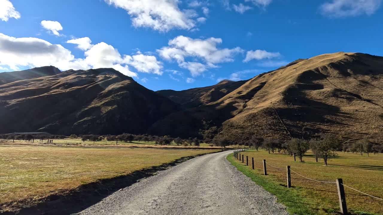Vehicle moves forward on rural gravel road, bright daylight, scenic mountains, wide angle perspective