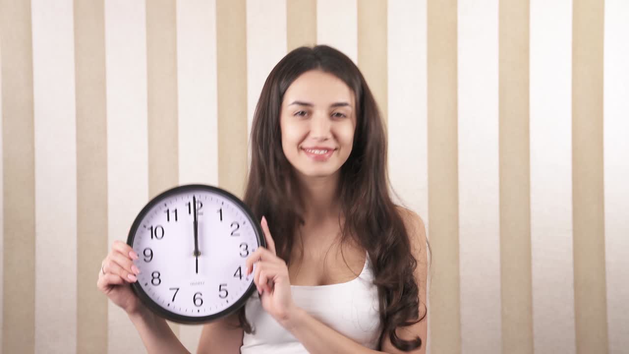 미소 짓는 행복한 소녀의 클로즈업, 그녀는 그녀의 손에 벽 시계를 회전, 그것은 정오입니다.