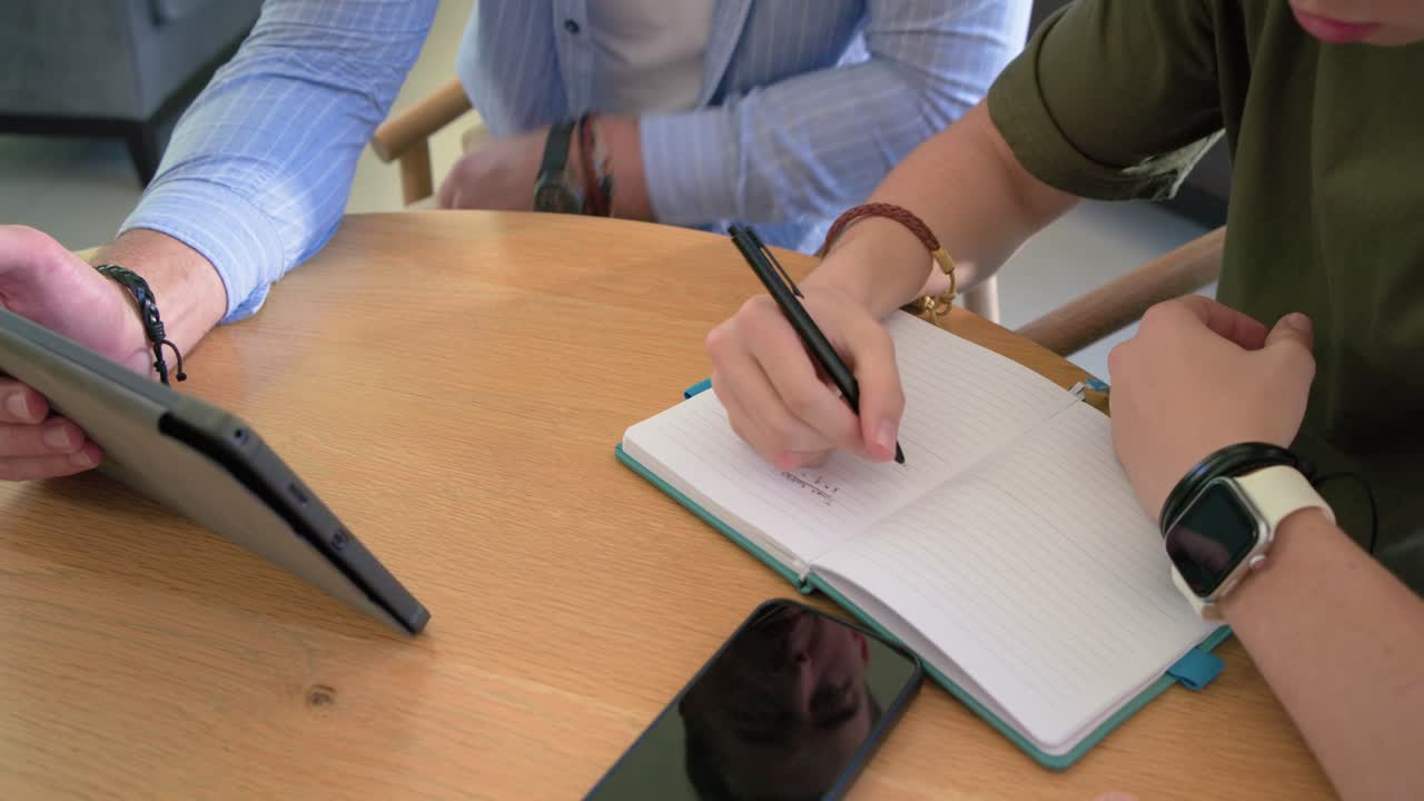 Tablet being angled toward notebook for tutoring, left hand pointing and right hand writing notes