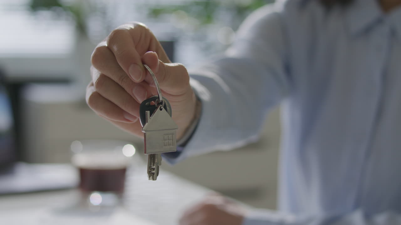 Hand of Real Estate Agent Holding House Shaped Keychain with Keys