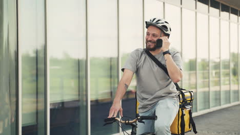 happy food delivery man wearing thermal backpack having a funny conversation on the phone on his bicycle