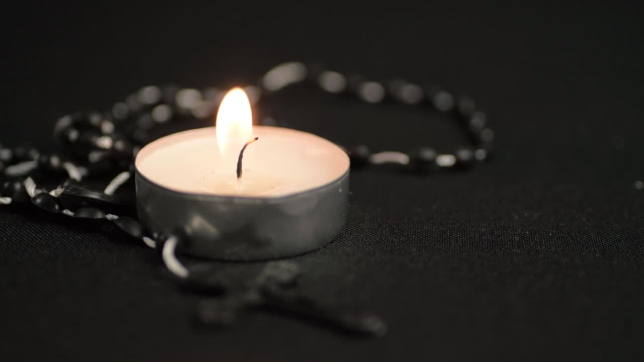 Single tea light with rosary bead close up on black background