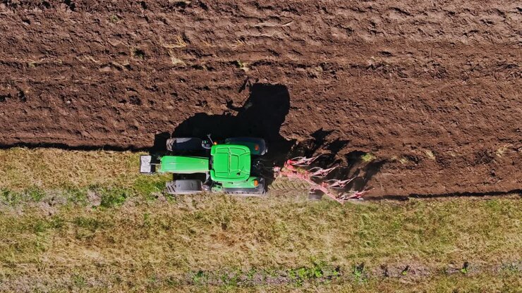 L'angolazione dall'alto rivela un trattore con un aratro rosso che solca il terreno mentre un drone ne segue il movimento