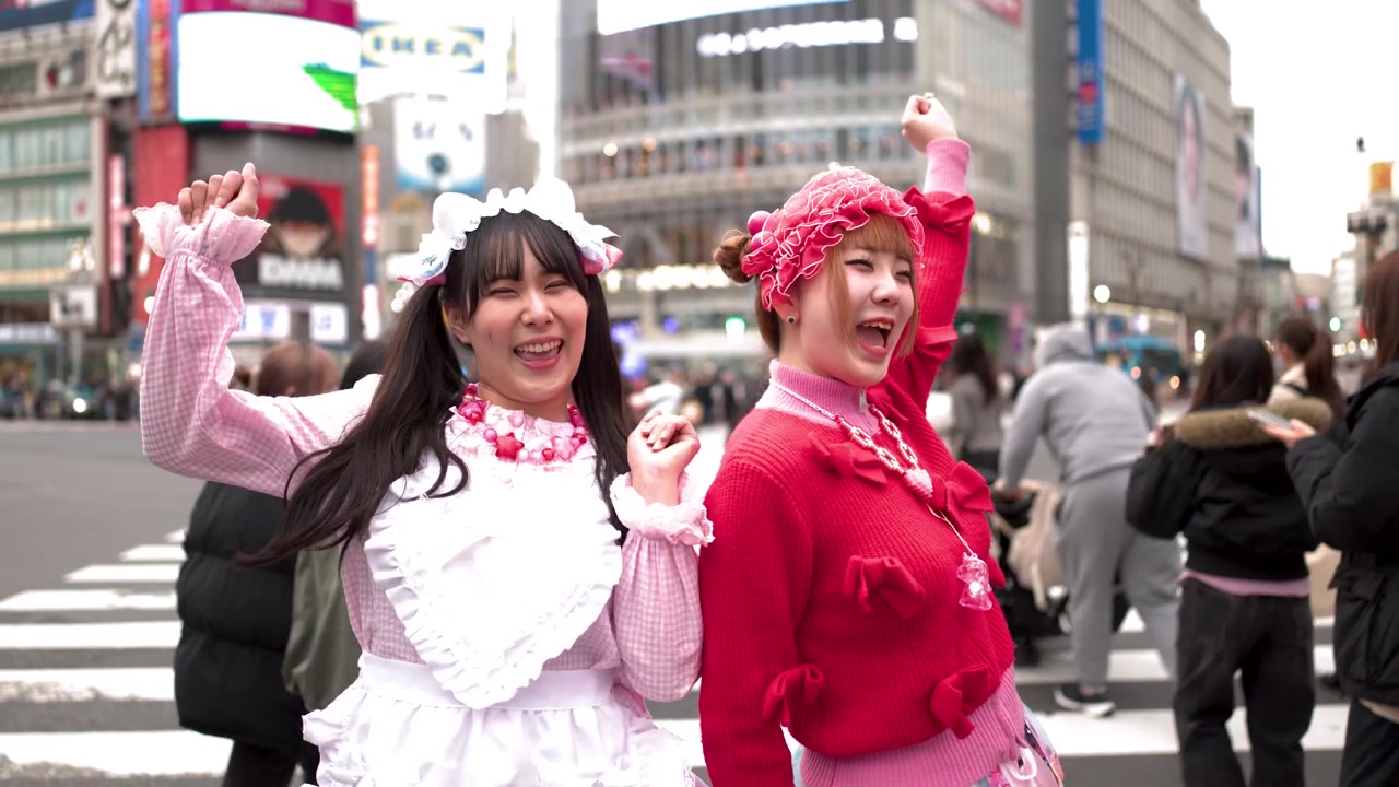 Due donne che indossano abiti colorati in stile decora ballano e ridono all'affollato incrocio di Shibuya.