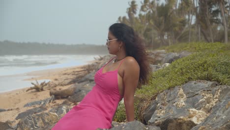 sexy modelo indio se sienta en las rocas de esta costa con olas rompiendo en la costa en cámara lenta