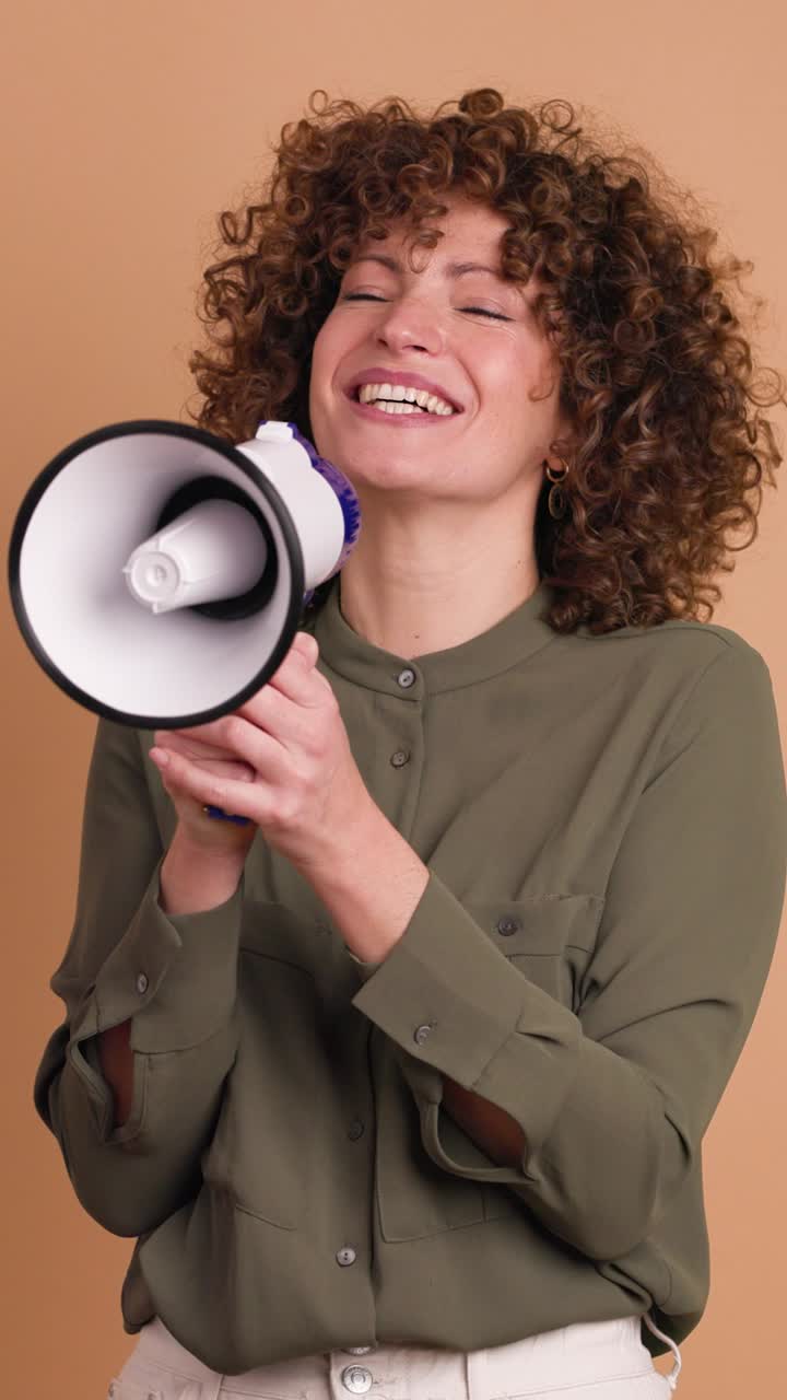 Excited young woman screaming on loudspeaker in beige studio. Vertical orientation