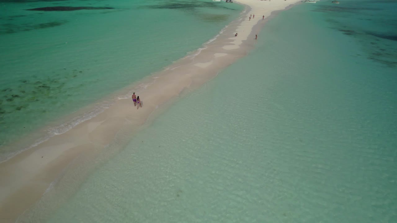 Aerial shot of a couple walking along a narrow sandbar, sea on both sides, Los Roques - Venezuela