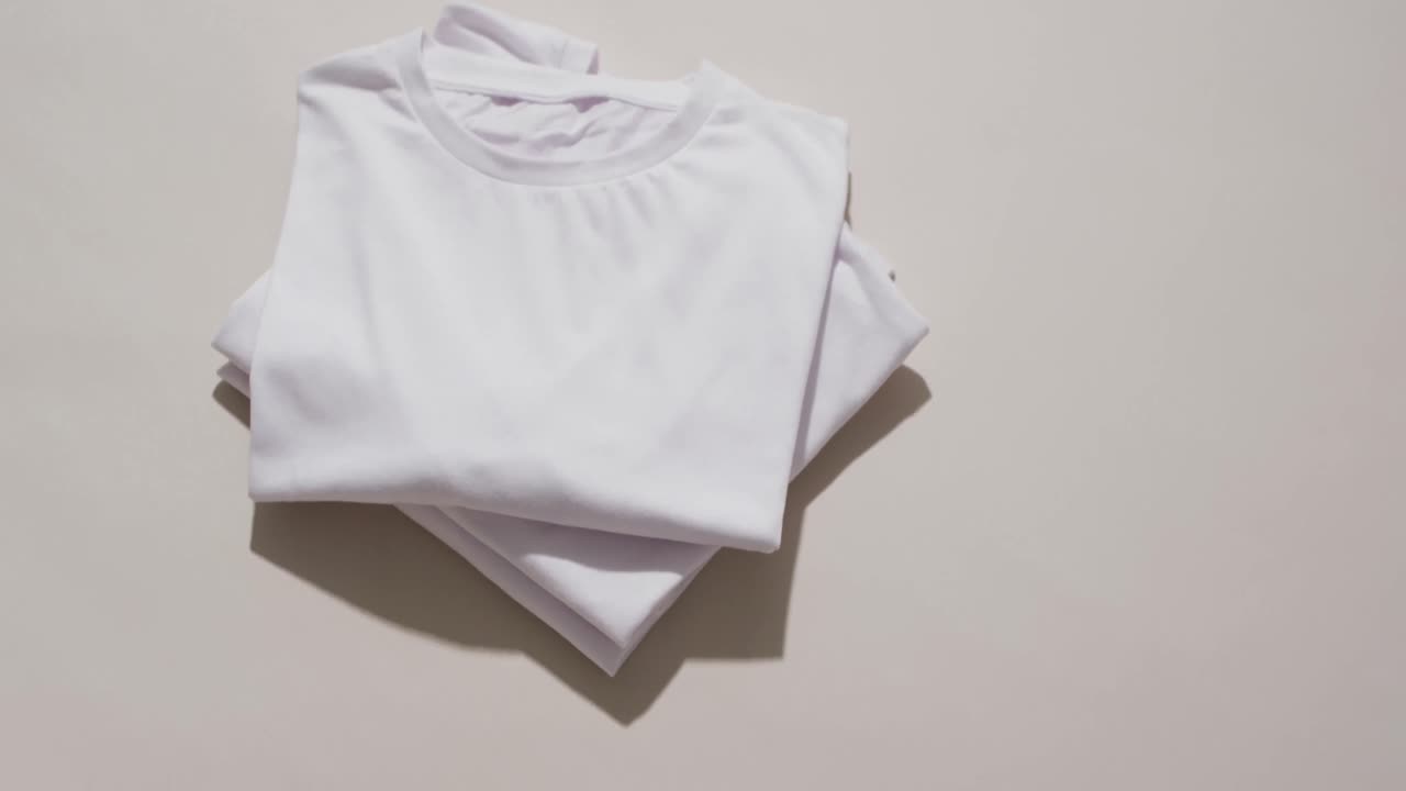 Video of stack of folded white t shirts with copy space on white background