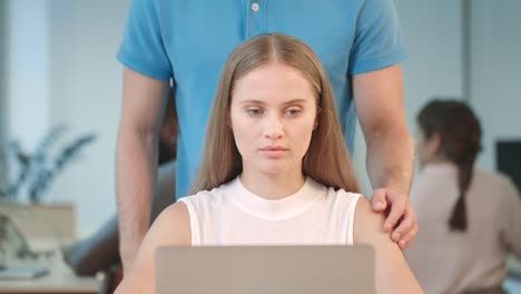 manos masculinas haciendo masaje a una mujer joven trabajando en una computadora portátil en un coworking