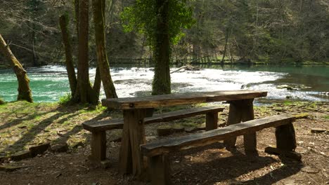 static shot of a small wooden picnic table at the side of the krka river