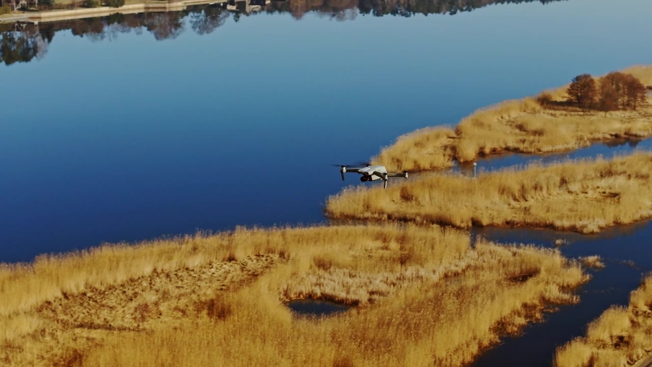 Luftovervågningsdrone patruljerer gyldent marskland ved siden af roligt blåt vand