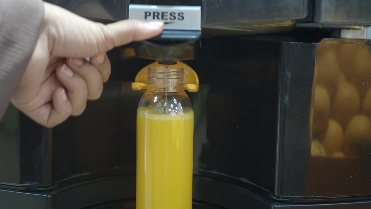 Una persona presionando un botón en una licuadora para obtener jugo de naranja