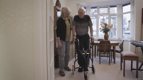 elderly man using a walker with a woman assisting him at home