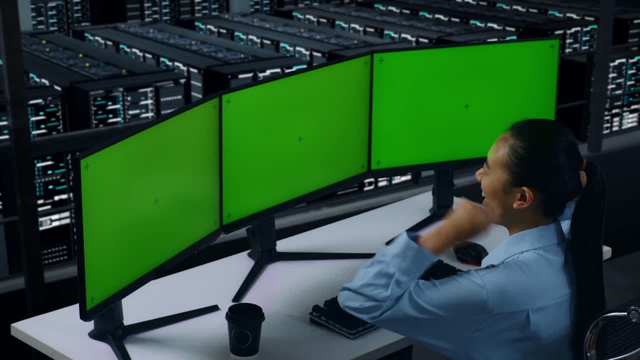 vista lateral de una feliz mujer asiática celebrando mientras trabaja con un simulacro de varios monitores de computadora en el centro de datos