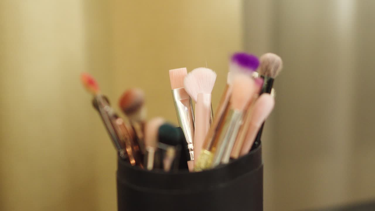 A woman's hand takes a makeup brush from a black container