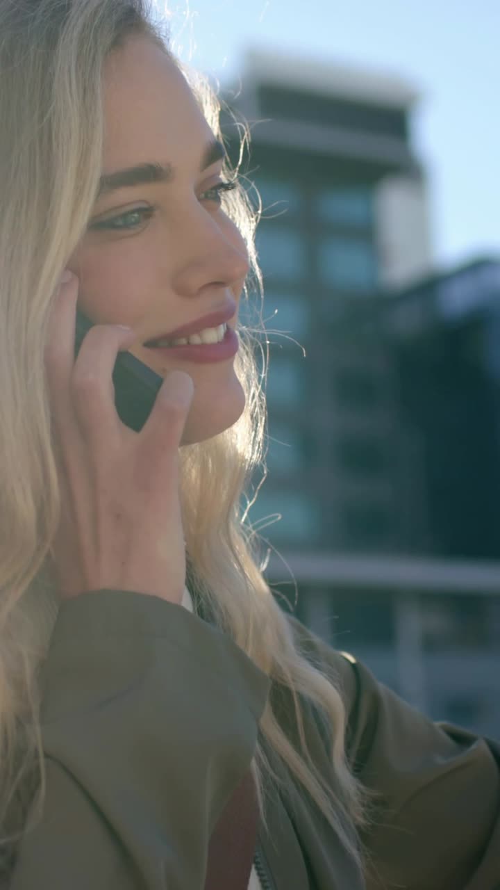 Video verticale: Donna sorridente con la giacca che tiene il telefono durante una chiamata vicino a un edificio, con spazio per il testo.