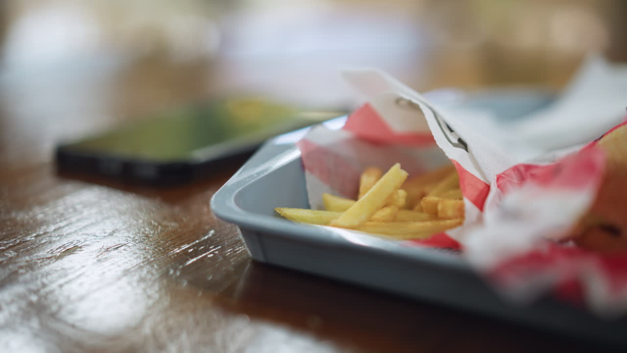 Person hand reaching into pile of crispy potato chips while camera captures closeup motion, focus on fingers and texture, casual snack moment with soft light reflecting on surface, and relatable scene