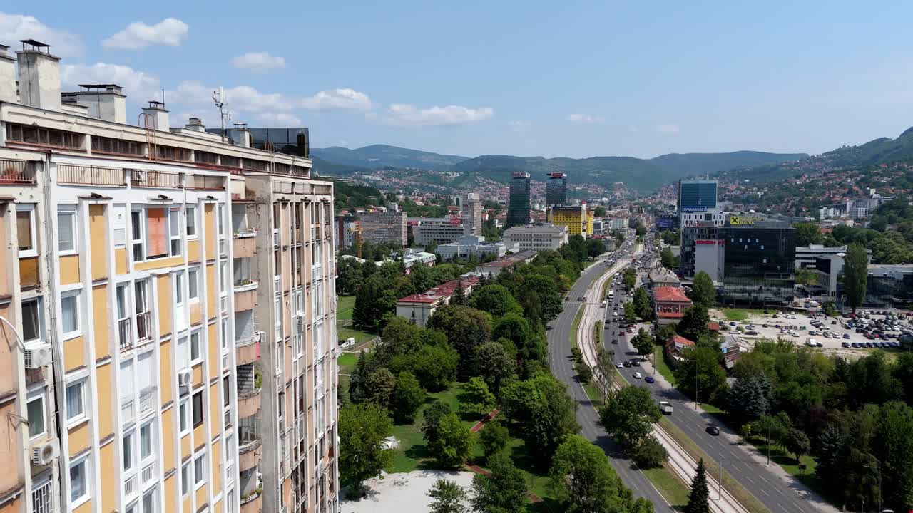 Aerial drone view of Sarajevo skyline, Bosnia and Herzegovina. Modern residential buildings, tree-lined boulevard, and distant mountains