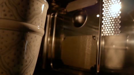 una taza pintada girando dentro de un microondas, reflejándose en un lado