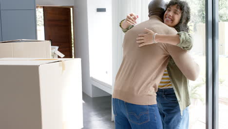 happy biracial couple embracing with cartons at new house, slow motion