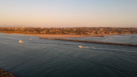 drone orbit around boats entering san diego mission beach harbor in the evening