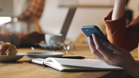 Woman-hand,-coffee-shop-and-phone-with-notebook