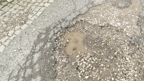 Rissige-Asphaltstraße-Mit-Schlagloch-Und-Pfütze