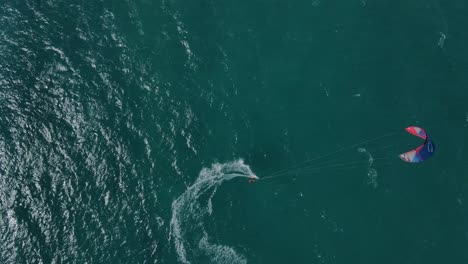 Aerial-overhead-flight-showing-kite-surfer-surfing-and-turning-on-clear-Pacific-Ocean-during-beautiful-weather-outside