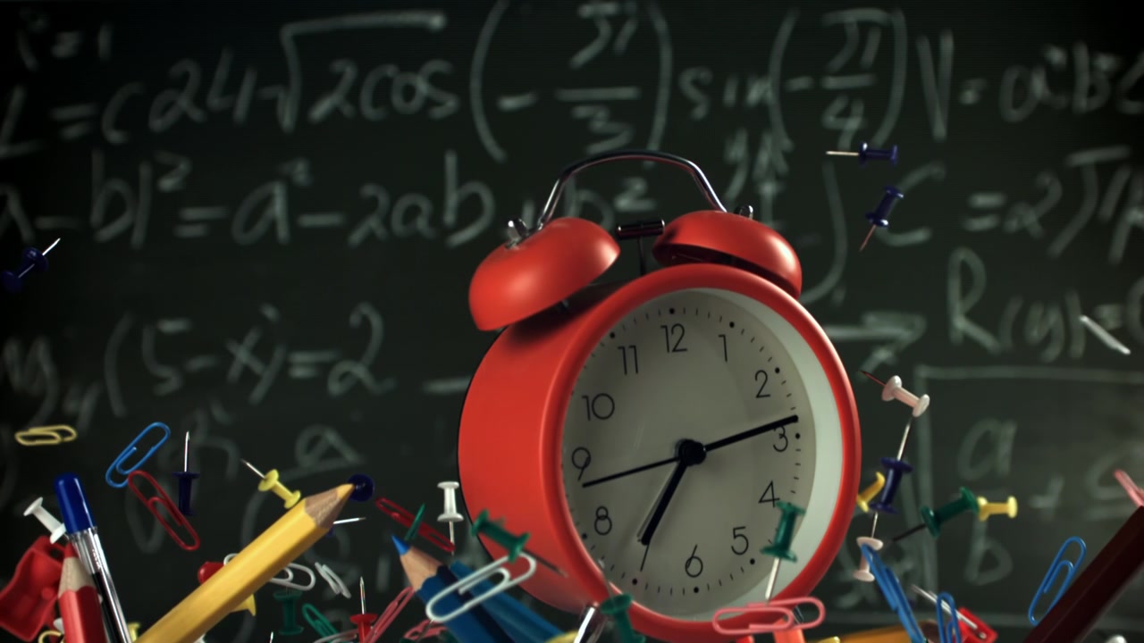 Koulutarvikkeita ja punainen herätyskello putoamassa matematiikan liitutaulua vasten.