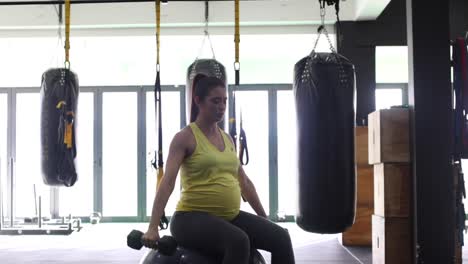 modelo femenino embarazada haciendo ejercicio con pesas en un gimnasio para mantenerse en forma en su cuarto trimestre