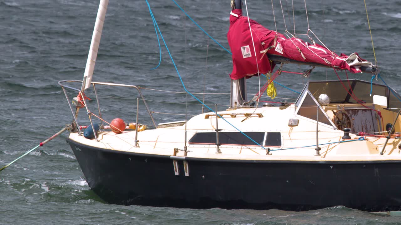 Sailboat anchored in choppy Cromarty Firth, Scotland, sways in strong wind, overcast daylight