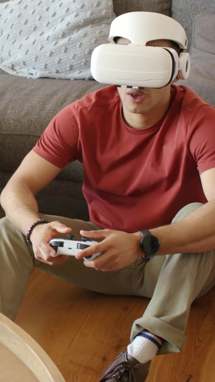 Vertical video: Reacting to game start, man in red tee with VR headset shifting controller at home