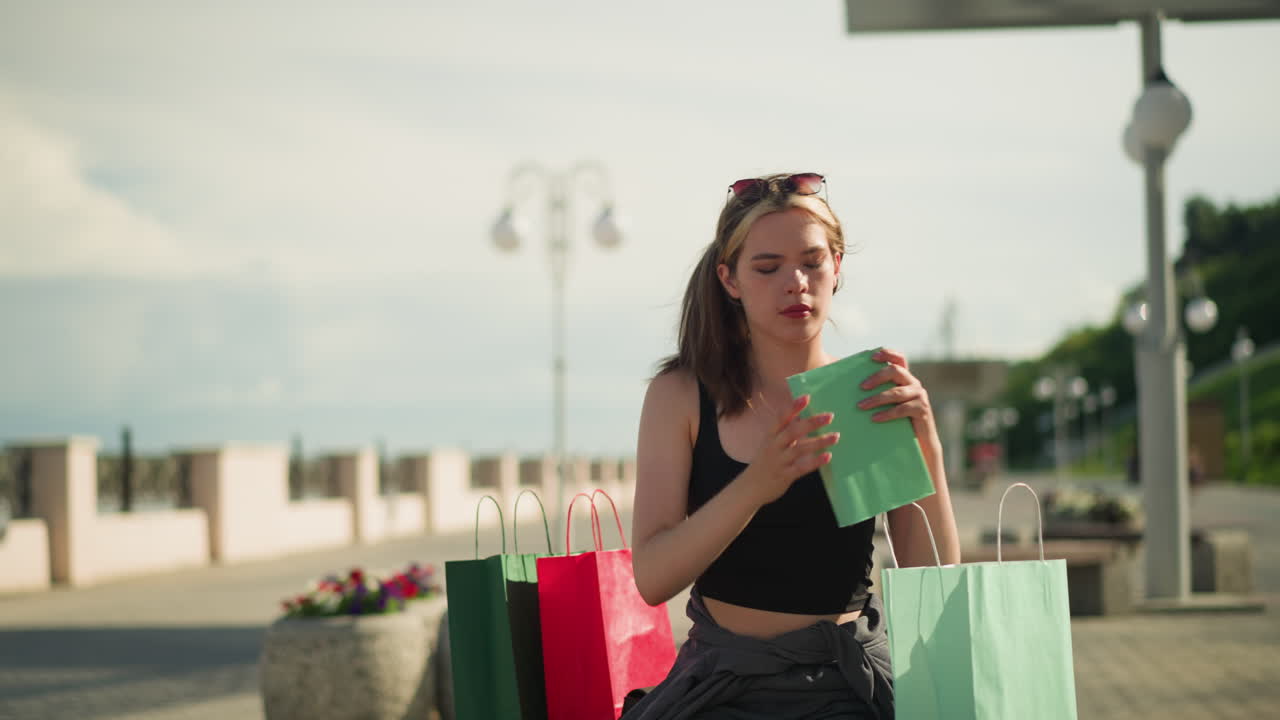 두 쪽 모두에 쇼핑 가방이 있는 야외 벤치에 앉아있는 여인이 민트 그린 가방에서 책을 가져오고, 그것을 열고, 페이지를 뒤집습니다. 배경에는 램프 기둥이 포함되어 있습니다.