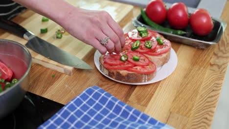 person preparing bruschetta with tomatoes and chili peppers in a kitchen