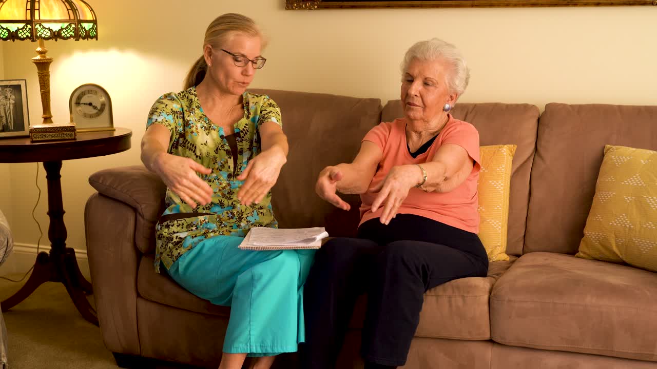Home healthcare nurse helping elderly woman with hand and wrist range of motion stretches