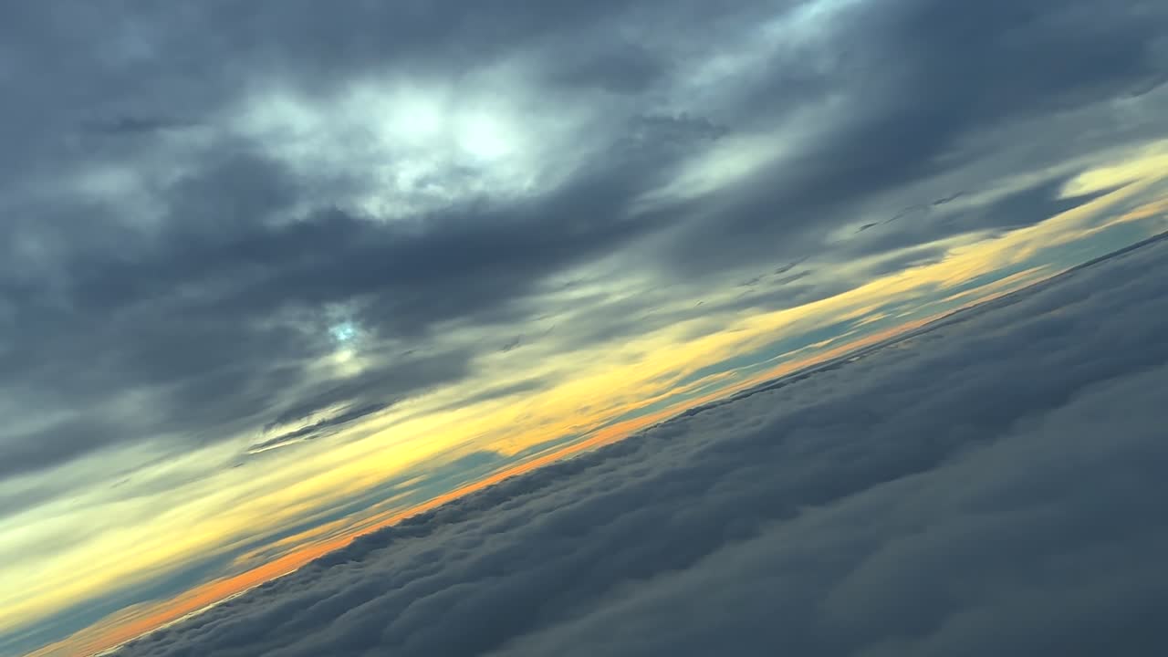 Pilotin silmin kuvattu oikealle kaartava lento harmaiden stratuspilvien lomassa auringonnousun aikaan, kultainen horisontti edessä.