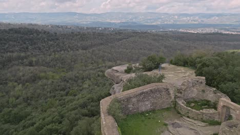 taradell castle ruins sit atop a large rock formation, surrounded by lush green forest, offering panoramic views of the catalan countryside