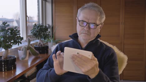 middle aged caucasian man is browsing the news on a tablet in a hobby room near a window with plants
