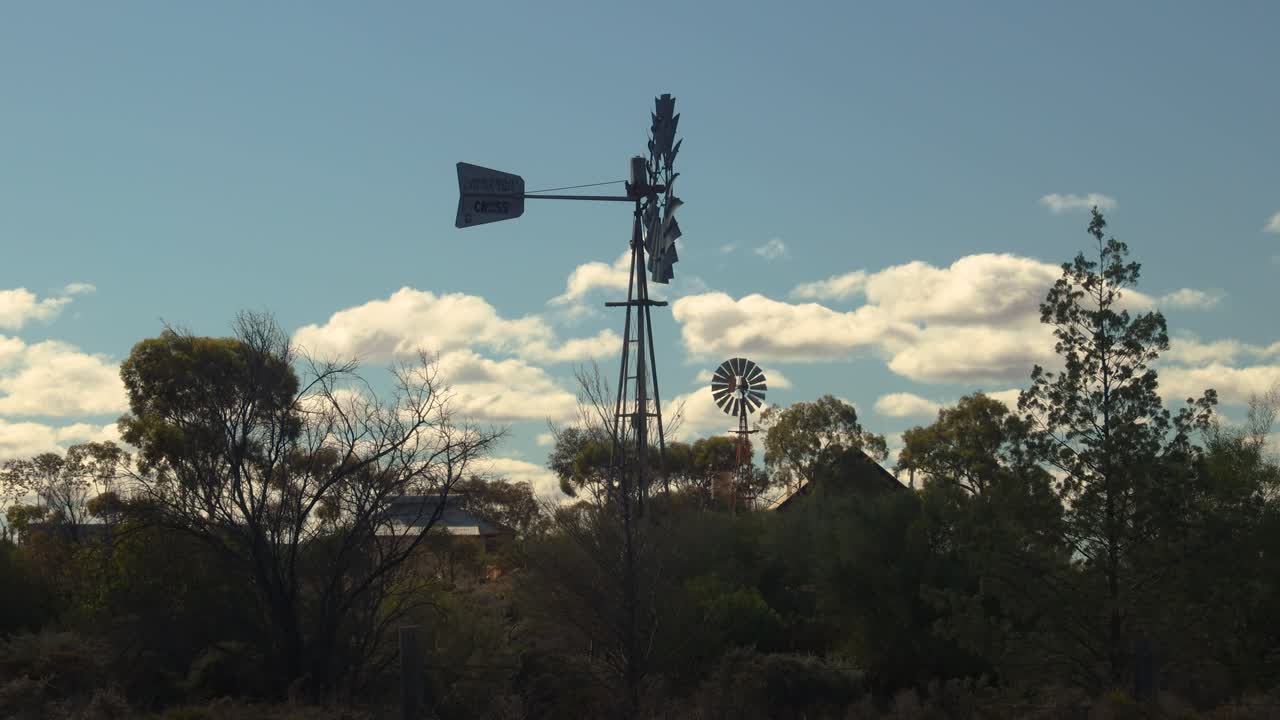 Majestic windmills stand silhouetted against a vibrant blue sky with fluffy clouds, capturing the serene beauty of the historic Beltana town in the South Australian Outback, Flinders Ranges.