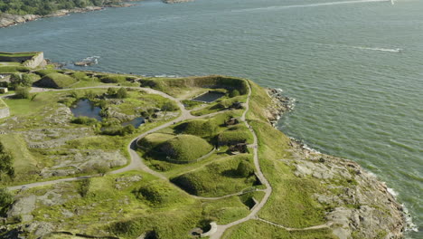 Aerial-view-overlooking-the-walls-and-the-south-coast-of-Suomenlinna-fortress-island,-on-a-sunny,-summer-day,-in-Helsinki,-Finland---Reverse,-drone-shot