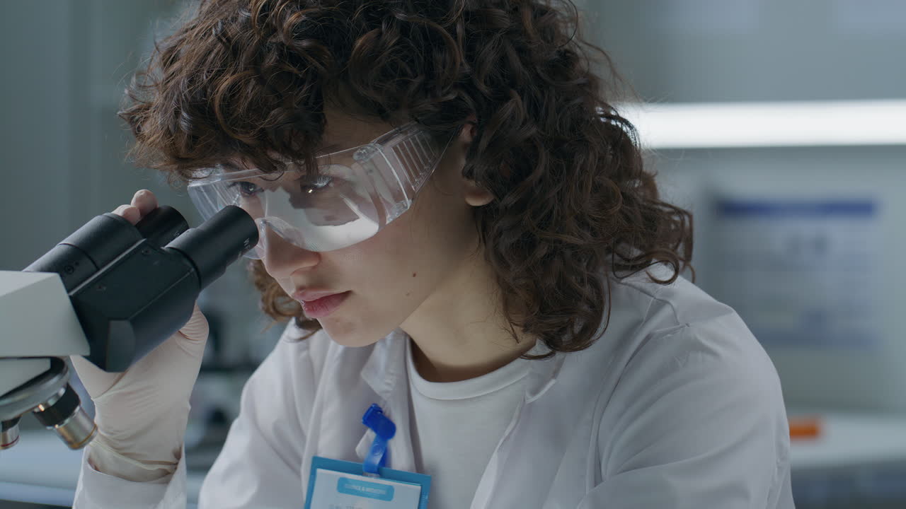 Young Female Researcher Looking through Microscope in Laboratory