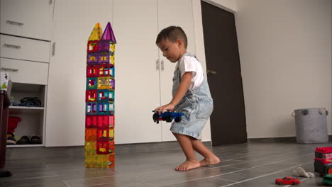 movimiento lento de un joven niño latino al lado de una torre hecha de azulejos magnéticos con coches de juguete en él sonriendo y levantando las cejas