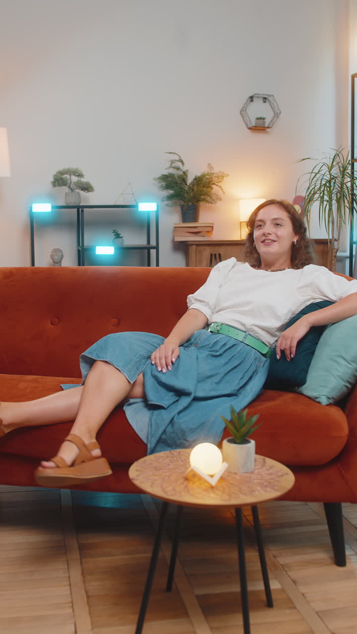 Happy carefree young caucasian woman sitting comfortably on sofa thinking in living room at home