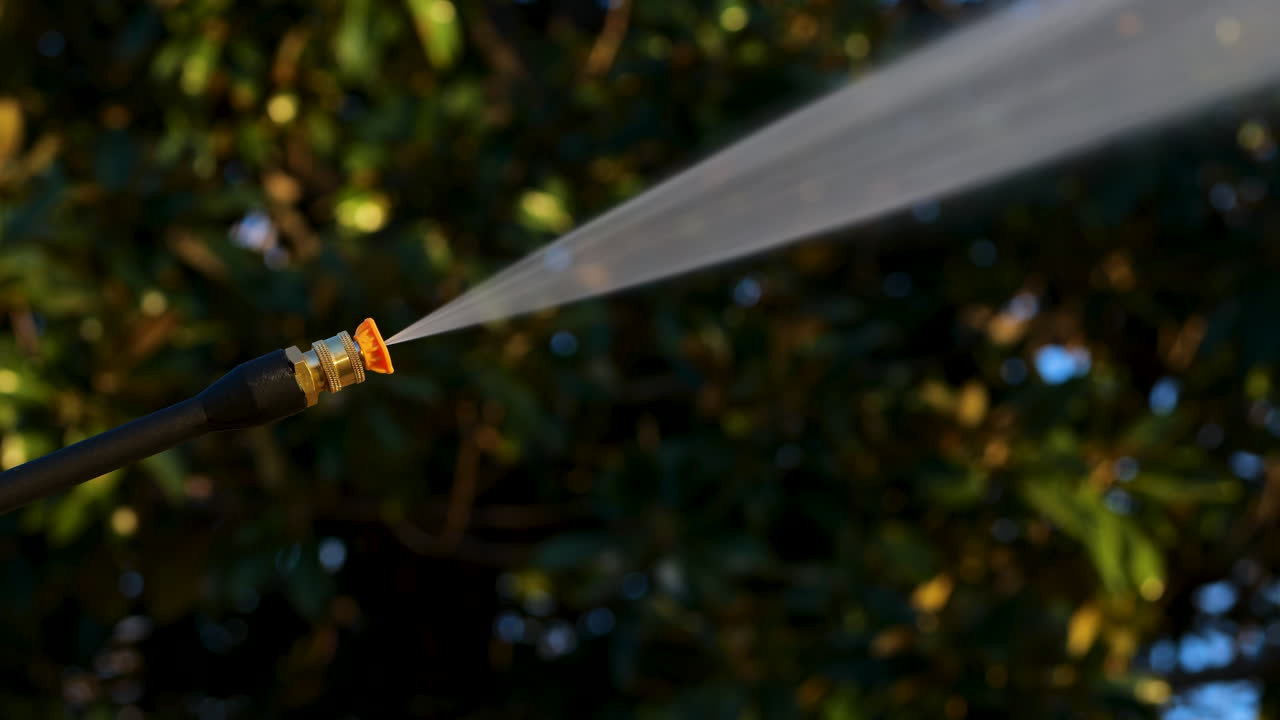 Power washer with yellow tip sprays high powered water jet with trees in background