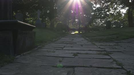 sunbeams over old churchyard pathway at sunset wide panning shot