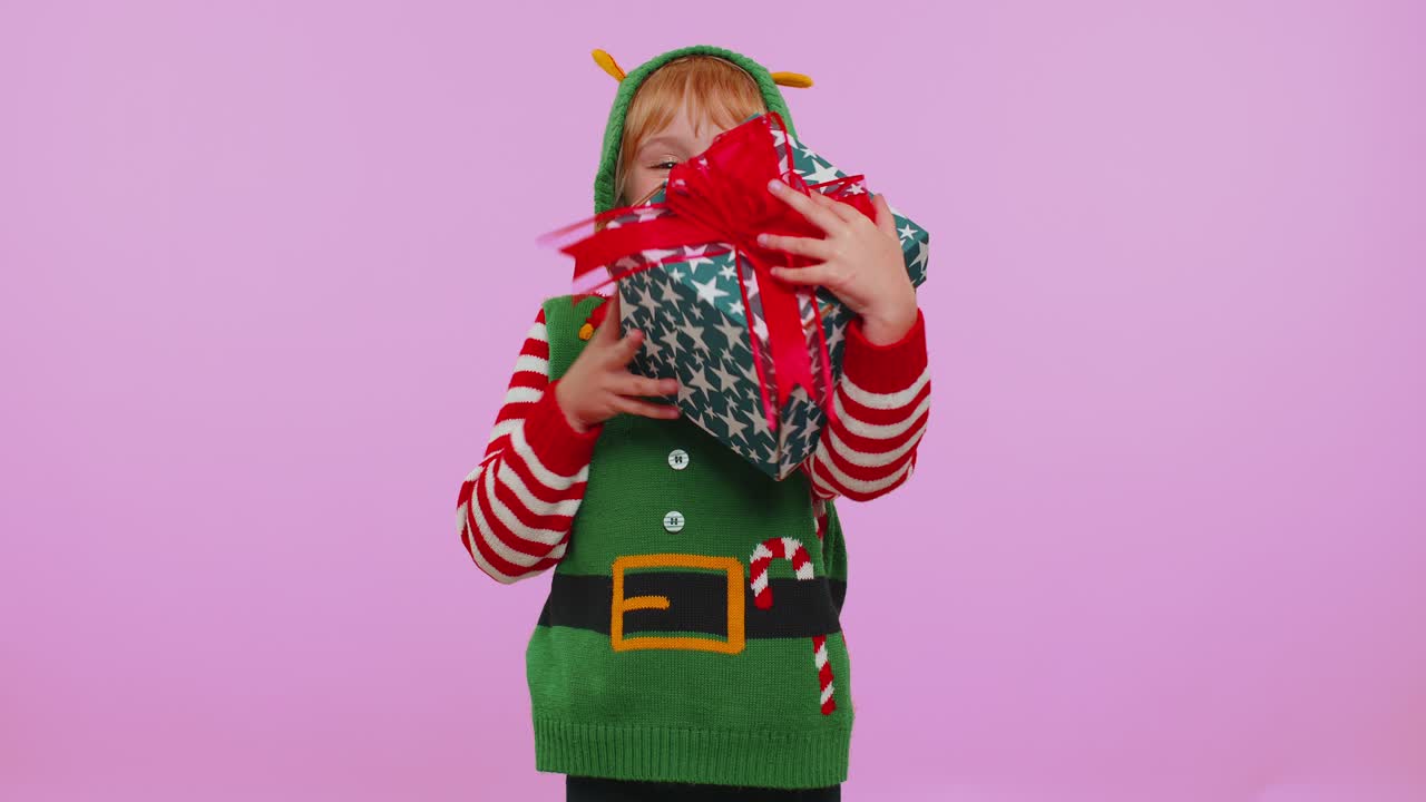 Veselá dívka v vánočním kostýmu Santa Clause dostala dárkovou krabici a vyjadřuje úžas a štěstí