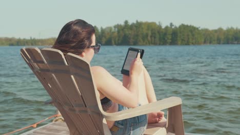 Mujer-Joven-Se-Relaja-En-Una-Silla-Adirondack-En-Un-Muelle-Junto-Al-Lago-En-El-Verano